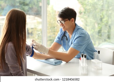 Doctor applying tourniquet on patient's hand for taking blood sample from vein in hospital
