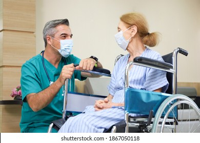 Doctor or assistance staff wear face mask and help or assist an elder patient woman while sitting on wheelchair in the hospital, coronavirus pandemic protection and healthcare encouragement concept