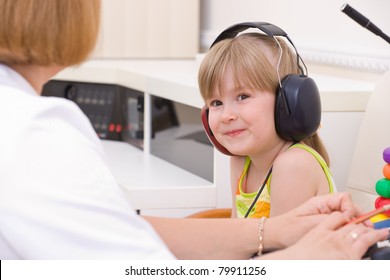 Doctor audiologist testing girl's ears on medical equipment