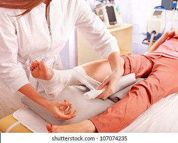 Doctor Bandaging Foot Patient In Hospital.