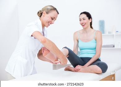 Doctor Bandaging Her Patient Ankle In Medical Office