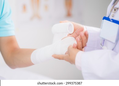 Doctor bandaging wrist of male patient with white bandage