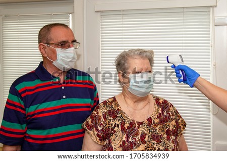 A doctor in blue latex gloves measures body temperature with an infrared emitter for a man and a woman aged.