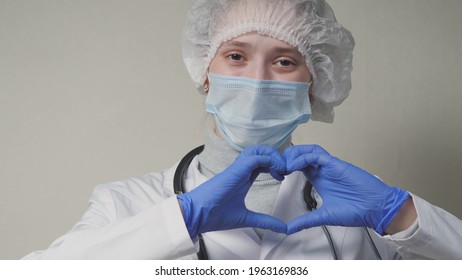 A Doctor In A Blue Mask And Gloves Smiles And Shows His Heart, A Professional Cardiologist In A Health Clinic, An Appointment With A Pediatrician In The Office, A Good Nurse, Coronavirus Pandemic