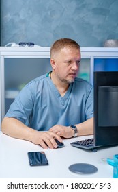 Doctor In Blue Scrubs Sitting Near Computer. Searching Medical Information. Diagnostic And Medical Concept.