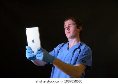 A Doctor In A Blue Uniform Holds A Digital Apple IPad In His Hands, Black Background - Moscow, Russia, May 1, 2021