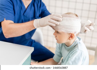 Doctor In Blue Uniform Touching A Boy Head With Trauma In His Head And Elastic Bandaged Around His Head.