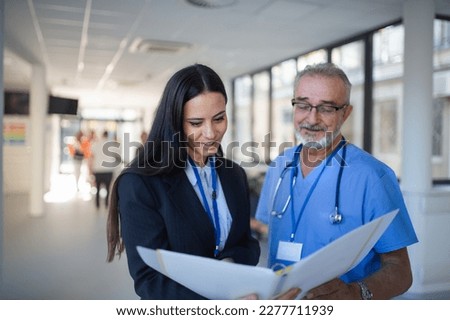 Doctor and business woman in hospital reading documents.