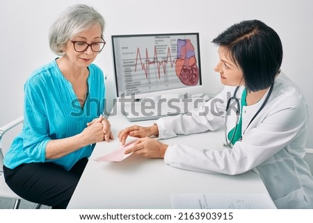 Doctor cardiologist analyzes heart electrocardiogram results of senior female while consultation. Diagnosis of heart rate and heart disease of older people