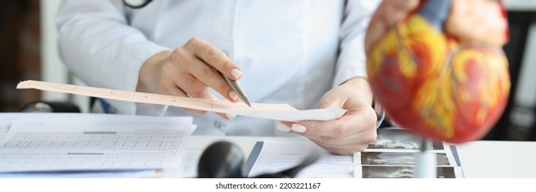 Doctor Cardiologist Examining Cardiogram Against Background Of Artificial Heart Model Closeup