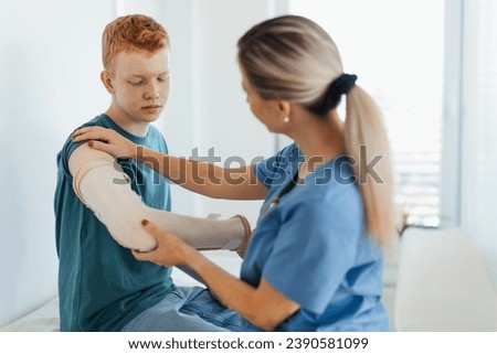 Doctor checking the orthopedic cast, brace on a teenage patient's broken arm. Teenage boy is healing a fracture after an accident.