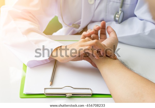Doctor is checking patience\'s pulse by\
fingers, medical checking on table. Asian\
doctor