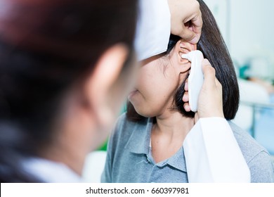 Doctor checking patient's temperature in the ear with Tympanic Thermometer, inside the clinic. Soft Focus. - Powered by Shutterstock