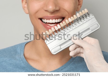 Doctor checking young man's teeth color on gray background, closeup. Dental veneers