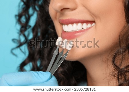 Doctor checking young woman's teeth color on light blue background, closeup. Dental veneers