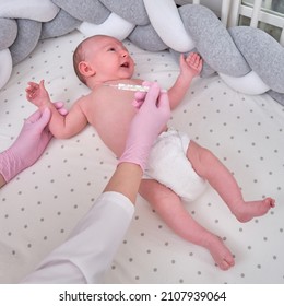 Doctor Checks The Temperature Of The Newborn Baby With A Thermometer. A Nurse In Uniform Measures The Child Fever With A Thermometer