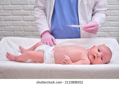 Doctor Checks The Temperature Of The Newborn Baby With A Thermometer. A Nurse In Uniform Measures The Child Fever With A Thermometer