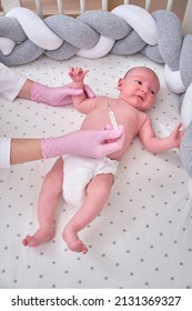 Doctor Checks The Temperature Of The Newborn Baby With A Thermometer. A Nurse In Uniform Measures The Child Fever With A Thermometer