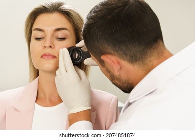 Doctor and client woman in dermatology clinic. Dermatologist is using dermatoscope for facial skin examination.