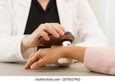 Doctor and client woman in dermatology clinic. Dermatologist is using dermatoscope for skin examination. - Powered by Shutterstock