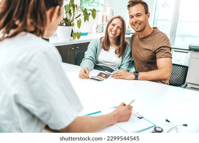 Doctor in clinic room showing ultrasound scan of baby to young couple - Gynecology consultation, pregnancy and artificial insemination concept - Powered by Shutterstock