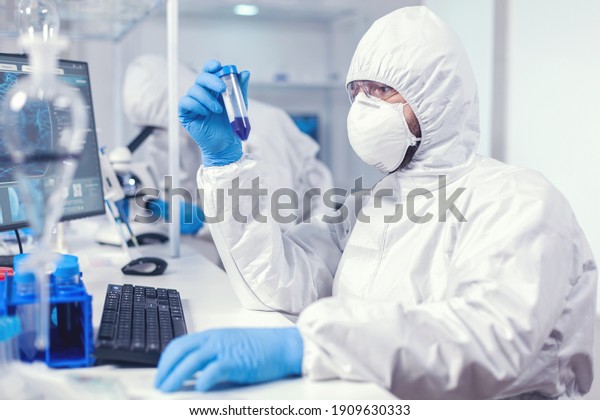 Doctor conducting scientific virus research\
holding test tube. wearing ppe suit. Scientist in laboratory\
wearing coverall doing research and analyzing substance during\
global pandemic with\
covid19.