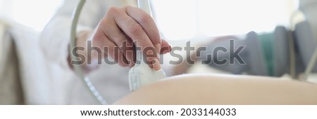 Doctor conducting ultrasound examination of fetus of pregnant woman in clinic closeup