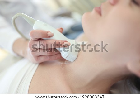 Doctor conducting ultrasound of thyroid gland to woman patient in clinic closeup