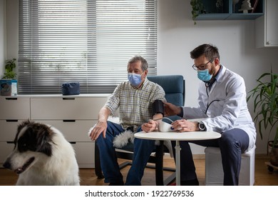 Doctor Consulting Elderly Male Patient At Home Dog In Foreground