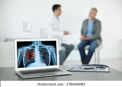 Doctor Consulting Man In Clinic, Blurred View. Focus On Laptop Displaying X-ray Of Patient With Lung Cancer