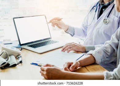 Doctor Consulting With Patient Presenting Results On Blank Screen Tablet Computer Sitting At Table