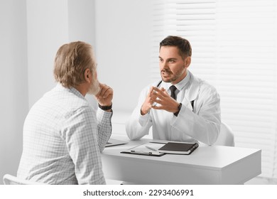 Doctor consulting senior patient at white table in clinic - Powered by Shutterstock