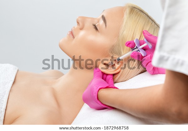 The doctor cosmetologist makes the injections
procedure for smoothing wrinkles and against flabbiness of the skin
on earlobe of a beautiful, young woman.Women's cosmetology in the
beauty salon.