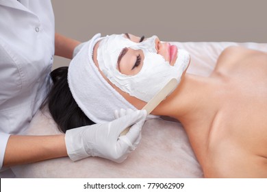 The Doctor Is A Cosmetologist For The Procedure Of Cleansing And Moisturizing The Skin, Applying A Mask With Stick To The Face Of A Young Woman In Beauty Salon.Cosmetology And Professional Skin Care.