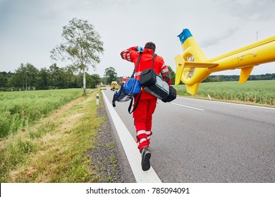 Doctor with defibrillator and other equipment running from helicopter. Teams of the Emergency medical service are responding to an traffic accident.