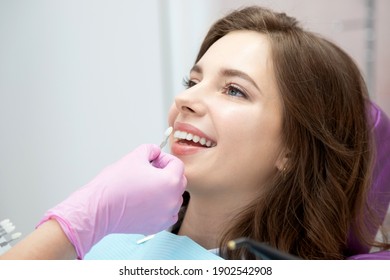 Doctor Dentist Selecting Teeth Enamel Shade Color For Young Positive Female Patient. Close Up Of Smiling Woman In Dental Chai On Stomatological Appointment. Dentistry And Stomatology Concept.