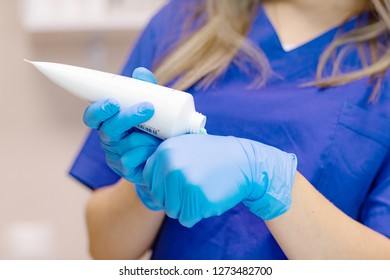 Doctor Dermatologist  Applies Cream From A Tube. Doctor Beautician Preparing To Apply Ointment Squeezes Out Of The Tube
