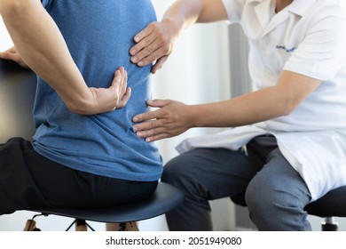 The doctor is diagnosing the patient's back pain. A male with back pain sees a doctor for treatment. - Powered by Shutterstock