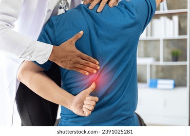 Doctor is diagnosing a patient's back pain in a hospital examination room. A male with back pain sees a doctor for treatment. - Powered by Shutterstock