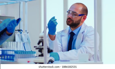 Doctor dictating to nurse virus results informations looking on test tubes in modern equipped laboratory. Doctors examining vaccine evolution using high tech researching diagnosis against covid19