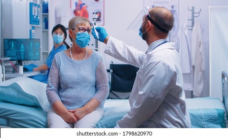Doctor dictating patient information to the nurse and she write it on the PC. Old retired senior woman wearing a mask and healthcare worker in protective equipment for consultation.