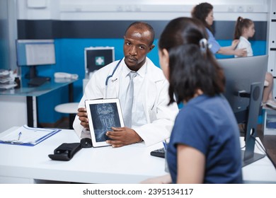 Doctor discussing x-ray scan of cervical spine injury diagnosis results and treatment with patient during medical appointment. Radiology medical exam in sterile antibacterial clinic environment. - Shutterstock ID 2395134117