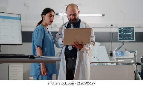 Doctor Doing Consultation With Retired Patient In Bed. Medic With Laptop Talking To Nurse About Healthcare Medicine Before Examining Patient With Nasal Oxygen Tube And Heart Rate Monitor