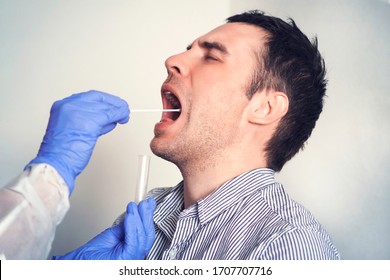 Doctor Doing Coronavirus Covid 19 Test For Male Patient. Taking A Saliva Sample From A Man. DNA Test. Collection Of Mucus From The Throat For Research In The Laboratory.