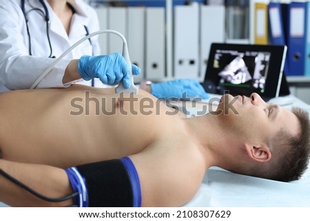 Doctor doing heart ultrasound to young male patient in clinic