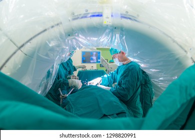 Doctor Doing Spine Surgery In Operating Room With Intra Operative Computer Tomography Machine. Shallow DOF With Blurred Foreground. Dramatic Light From Tunnel Of CT Device. Medical Concept.