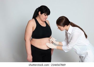 Doctor Drawing Marks On Obese Woman's Body Against Light Background. Weight Loss Surgery