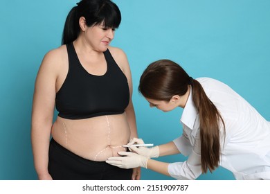 Doctor Drawing Marks On Obese Woman's Body Against Light Blue Background. Weight Loss Surgery