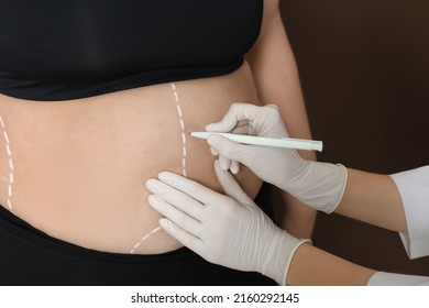 Doctor Drawing Marks On Obese Woman's Body Against Brown Background, Closeup. Weight Loss Surgery