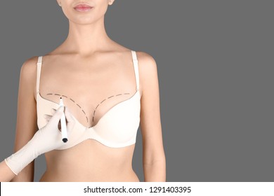 Doctor drawing marks on patient's breast for cosmetic surgery operation against gray background, closeup. Space for text